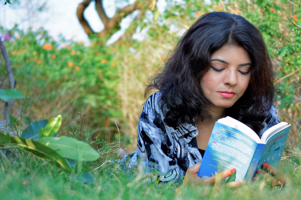 Photo of Saima Afreen reading a book while laying in the grass