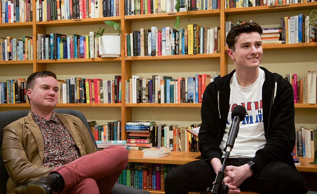 Two young people sitting by a book shelf