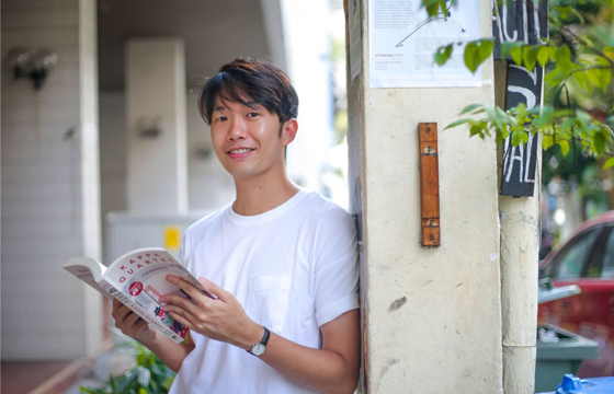 Photo of Daryl Yam leaning against a wall holding a book