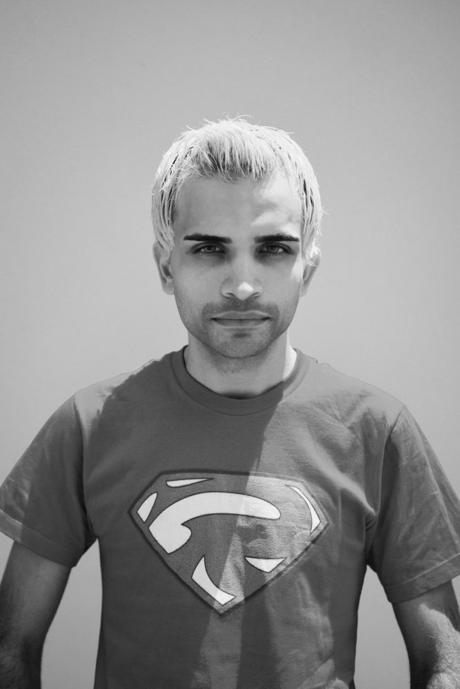 A black and white portrait of Raphael Farmer. He is wearing a superman t-shirt and smiling. 