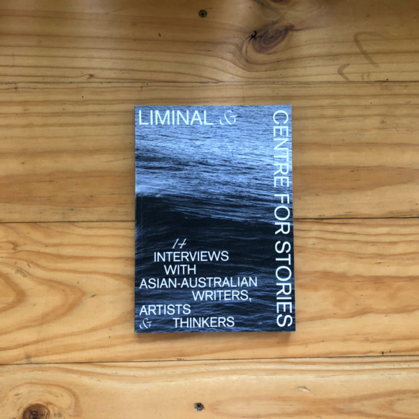 A photograph of a book on top of a light coloured woodern table. The book cover is black and white featuring an image of an ocean and it says 'LIMINAL & CENTRE FOR STORIES Interviews with Asian Australians'