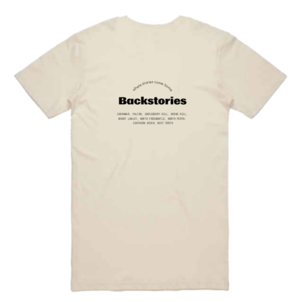 A photograph of a t-shirt. It's a natural sandy colour. On the back is the bold black logo for Backstories. Under it is the suburbs that each backstories event is located at. Above in a rainbow shape is the slogan 'where stories come home'