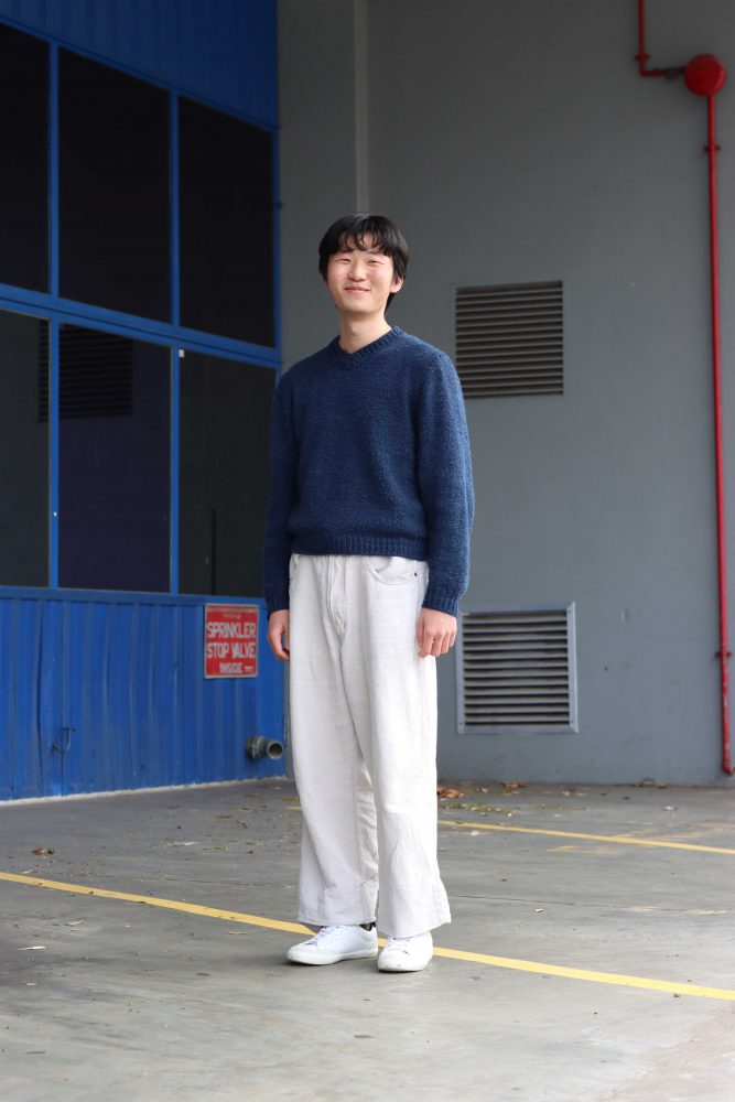 You can see Luoyang standing in front of a grey and blue wall. He is smiling at the camera.