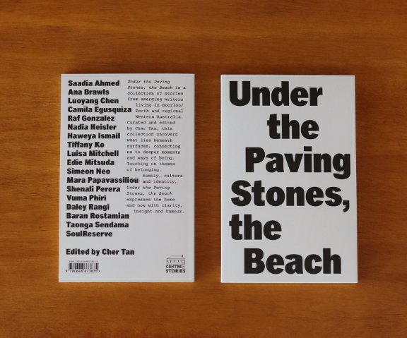 A photo of the book Under the Paving Stones the Beach laying down so that you can see the front and back cover. On the front cover it simply says 'Under the Paving Stones the Beach' in bold font on a plain cream background. On the back cover is the authors names and blurb which is not in focus.
