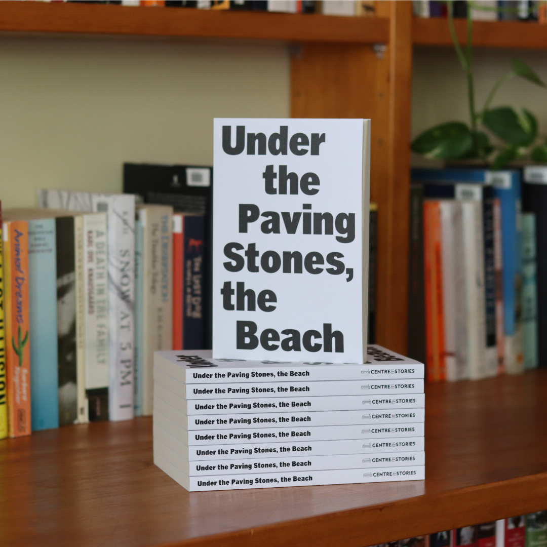 A photograph of a book. The book is a natural beige colour with bold black writing covering the entire cover page. The writing says 'Under the Paving Stones, the Beach'